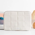 Detailed view of cream quilted laptop sleeve with branded patch in home office setting - 14" / Beige