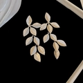 Detalle macro de pendientes de hoja dorada con texturas de vetas sobre fondo negro - Estilo de Borla de Hoja de Pin de Plata / Plateado