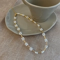 Detailed view of elegant gold pearl flower necklace next to a ceramic coffee cup - Gold Pearl Flower Necklace