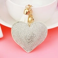 Detalle de llavero de cuero en forma de corazón con pedrería, cascabel y borla blanca - Tono Dorado + Base Blanca Con Diamantes de Imitación Transparentes