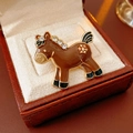 Détail macro d'une broche cheval vintage en émail avec cristaux dans un écrin en cuir - Marron