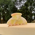 Close-up of a marble-textured acetate hair claw with gold label on a wooden railing - Pink Yellow