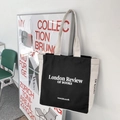 Detail of a black and white canvas tote bag with literary text hanging on a white wall - Black