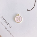 Macro detail of round pink enamel letter N pendant with gold metal trim for DIY jewelry - Letter N