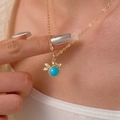 Detailaufnahme einer goldenen Vogel-Halskette mit Türkis-Anhänger am Hals eines Models - Vogel und Blatt Halskette mit Blauem Hauptstein (7834) / KC Gold