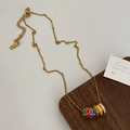 Close-up of gold chain necklace with seven colorful enamel beads on wooden display - Multicolor Multi-Hoop Pendant Necklace