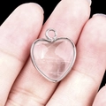 Pink heart crystal pendant in silver frame held by hand against black background - Clear Quartz Silver Edging