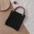 Detail of black knit tote bag showing cable knit texture and brown wooden handle - Black
