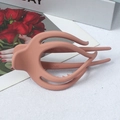Pince à cheveux mate orange corail au design profilé posée sur un magazine de mode - Rose Poudré Mat