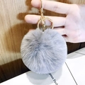 Gray plush heart keychain featuring a golden metal ring held against a wooden background - Small Grey Pom Pom
