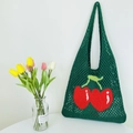 Close-up of green knitted mesh tote bag featuring a vibrant red cherry pattern design - Green