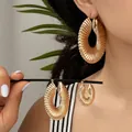 Set di orecchini a cerchio dorati con texture a spirale in tre misure su modella e mano - Giallo Oro
