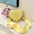 Detail of yellow heart-shaped bag with litchi texture and wide lettered shoulder strap - Yellow
