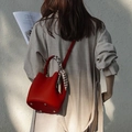 Detail of red leather bucket bag with silk scarf on handle shown in lifestyle setting - Red