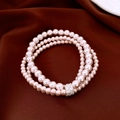 Macro detail of triple-layer pearl bracelet with rhinestone clasp on brown silk - Three-layer Stacked Pink Pearl Style