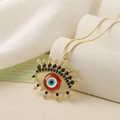 Collier avec pendentif œil doré, pierre rouge et zircons noirs sur support blanc - Œil Rouge