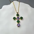 Detailed shot of golden cross pendant with green and purple gemstones on ceramic tray - Purple and Green Cross