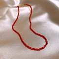 Elegant red faceted bead necklace with gold clasp laid on soft beige silk fabric - Red Faceted Bead Strand Necklace