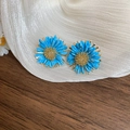 Vue macro de boucles d'oreilles marguerites en raphia bleu avec centre doré sur tissu - Bleu