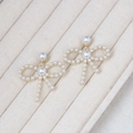 Detailed view of bowknot pearl earrings with gold base on a textured jewelry display tray - Gold Bow Pearl Full Rhinestone Studs
