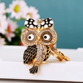 Macro shot of owl keychain with sparkling crystals and black enamel on floral background - Bow Owl Black