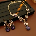 Detalle del conjunto de joyas doradas con cristales púrpura sobre terciopelo negro - Set de collar y pendientes / Morado