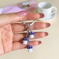 Handheld view of colorful resin mushroom keychain with blue spotted charms and metal ring - Deep purple