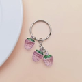 Detail eines silbernen Schlüsselanhängers mit drei lila Erdbeeren auf rosa Hintergrund - Lila Erdbeere (Ohne Verschluss)