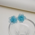 Macro view of sky blue matte translucent floral earrings on a glass edge - Blue