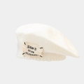 Detailed view of cream knitted beret featuring a vintage cloth patch with stitched letters - One Size / White
