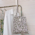Close-up of floral canvas tote bag with white tag detail on white shirt background - Light Grey with White Gardenia