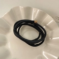 Detail of a minimalist black faux leather hair tie with gold metal tips on a ceramic plate - Black