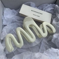 Close-up of wavy cream-white resin hair claw clip on soft tissue paper packaging - Beige