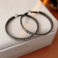 Vista macro de pendientes de aro de cuero negro con diseño de letras blancas en terciopelo - Negro