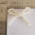 Detalle de accesorio lazo de perlas DIY con medidas 4,2cm x 3,8cm sobre escala - Lazo beige pequeño / 5cm x 3cm