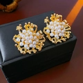 Primer plano detallado de pendientes de flores doradas con perlas sobre estuche negro - Estilo de Flor con Aguja de Plata / Dorado