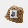 Close-up of brown chunky knit bucket hat featuring a white square patch with abstract art - Khaki
