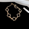 Detail shot of golden clover flower chain bracelet on elegant white fabric background - Bracelet - Gold - Flower