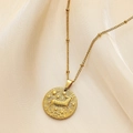 Close-up of golden Aries zodiac coin pendant with small bead chain on silk background - Aries
