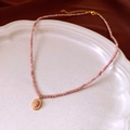 Detail of pink beaded necklace with gold oval pendant on a decorative white porcelain plate - Necklace-Pink