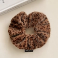 Dettaglio di scrunchie felpato con stampa leopardata ed etichetta nera su fondo bianco - Leopardo Marrone