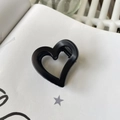 Dettaglio di un mollettone nero opaco a forma di cuore su una pagina di libro bianco - Circa 4,2 cm / Nero opaco