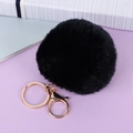 Close-up of black faux fur pompom keychain with golden metal ring on purple background - Black