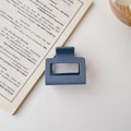 Close-up of a matte blue square hair claw clip placed on an open book with minimalist aesthetic - Matte Haze Blue