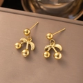 Detail of gold cherry earrings with metallic sphere dangles on brown leather surface - Minimalist Cherry / Gold