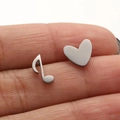 Macro shot of asymmetric music note and heart stud earrings held on a fingertip - Steel