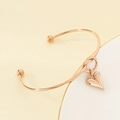 Detail eines roségoldenen Herzanhänger-Armreifs mit Perlenenden auf beige-weißem Grund - Roségold