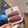 Close-up of two purple cashmere teardrop clips with beaded edges on a display card - Purple