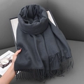 Deep grey cashmere-like scarf with fringe detail held against a cozy sofa background - 68x180cm / Dark Grey Green