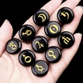 Polished black stones engraved with golden solar system planet symbols in hand - Obsidian